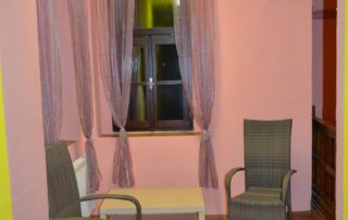 menší místnost vymalovaná růžovou barvou, konferenční stolek, dvě proutěná křesla šedé barvy