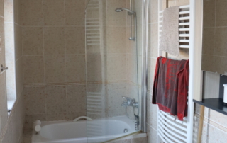 koupelna s béžovým obložením s vanou v pozadí, žebříkovým topením a umyvadlem v popředí