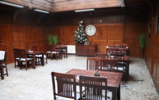 prostorná místnost s dřevem obloženými stěnami, střešními okny a šedou dlažbou vybavená dřevěnými stoly a židlemi v tmavém odstínu, v pozadí vánoční stromek