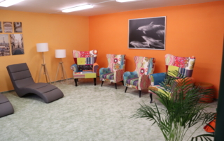 Místnost s oranžovými stěnami a barevnými křesílky, po levé straně relaxační šedá lehátka